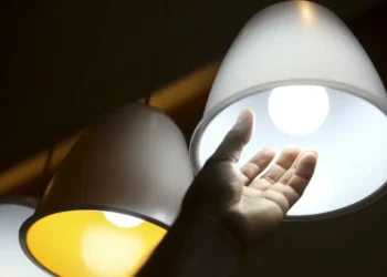 Mão próxima de lâmpada acesa, simbolizando consumo de energia elétrica