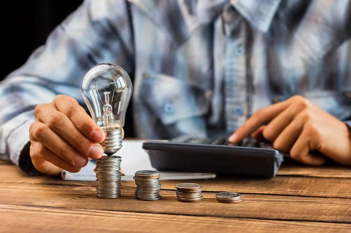 Pessoa segurando lâmpada sobre moedas empilhadas, representando economia de energia