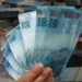 Notas de 100 reais em destaque, representando um tema de ressarcimento financeiro e pagamentos.