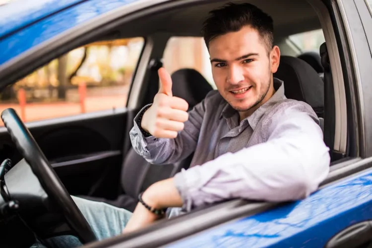 Jovem sorrindo e fazendo sinal de positivo dentro de um carro, representando a participação no Programa Escola de Motoristas.