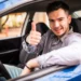 Jovem sorrindo e fazendo sinal de positivo dentro de um carro, representando a participação no Programa Escola de Motoristas.