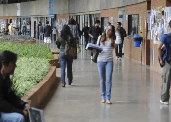 Estudantes circulando por corredor de instituição de ensino com mochilas e materiais