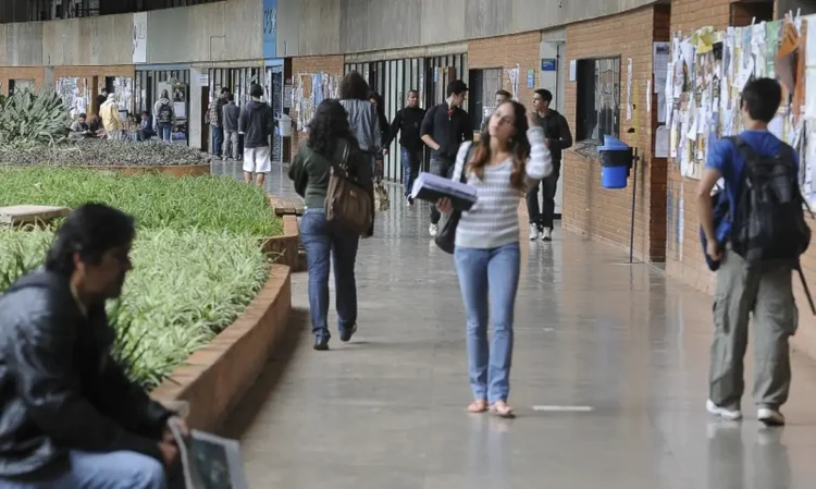 Estudantes circulando por corredor de instituição de ensino com mochilas e materiais