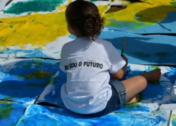 Criança pinta o chão com cores vibrantes usando camiseta com a frase “Eu sou o futuro”