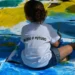 Criança pinta o chão com cores vibrantes usando camiseta com a frase “Eu sou o futuro”