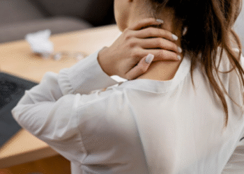 Mulher com dor no pescoço em ambiente de trabalho, indicando sintomas de fibromialgia