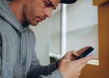 Homem usando celular com expressão desconfiada, alerta para possíveis golpes
