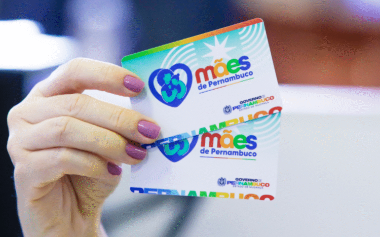 Cartão do Programa Mães de Pernambuco sendo segurado por uma mão com unhas pintadas, destacando o apoio às mães no estado.