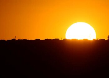 Sol se pondo no horizonte com céu alaranjado ao fundo de uma cidade