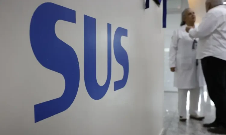 Profissionais conversando em unidade de saúde com o logo do SUS em destaque