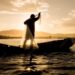 Pescador recolhendo rede ao pôr do sol durante o período de defeso
