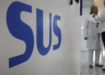 Logo do SUS em parede de unidade de saúde com profissionais ao fundo