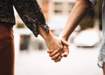 Casal segurando as mãos em um gesto de união estável, com fundo urbano desfocado.
