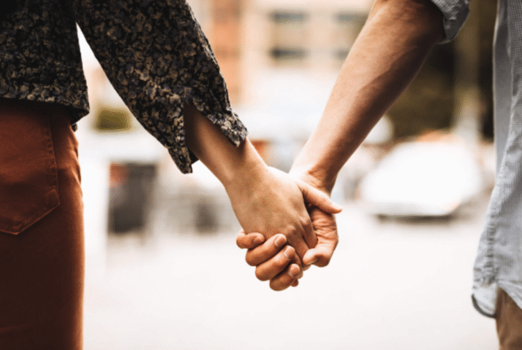 Casal segurando as mãos em um gesto de união estável, com fundo urbano desfocado.