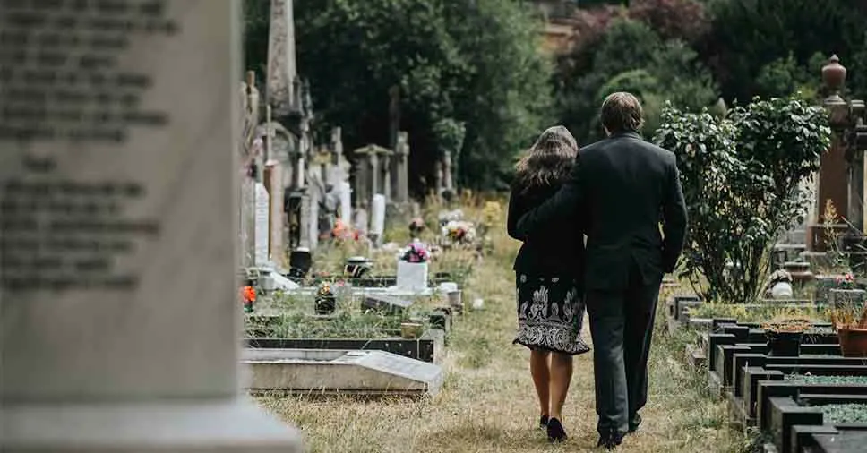 Casal caminhando em um cemitério, simbolizando a reflexão sobre os ativos invisíveis que não foram resgatados após a morte de um ente querido, como benefícios e saldos bancários não transferidos.