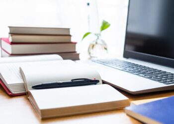 Imagem de uma mesa de trabalho com livros, caderno e laptop, simbolizando a iniciativa 'Seu Primeiro Passo' que oferece cursos gratuitos CadÚnico para jovens em 2025.