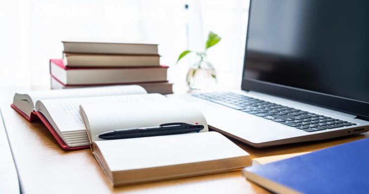 Imagem de uma mesa de trabalho com livros, caderno e laptop, simbolizando a iniciativa 'Seu Primeiro Passo' que oferece cursos gratuitos CadÚnico para jovens em 2025.