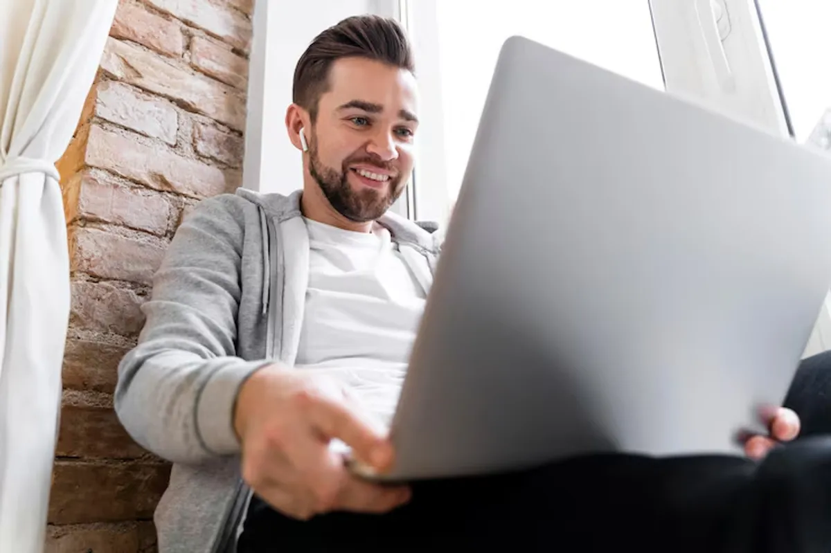 Homem sorrindo enquanto usa um laptop, ouvindo música com fones de ouvido.