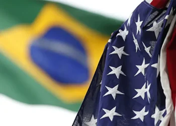 Bandeira dos Estados Unidos em primeiro plano com a bandeira do Brasil ao fundo, simbolizando os impactos do tarifaço americano nos preços e no cotidiano.
