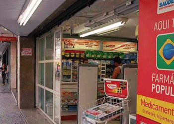 Entrada de farmácia com aviso do programa Farmácia Popular do Brasil, destacando medicamentos gratuitos para diabetes e hipertensão.