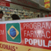 Interior de uma farmácia com foco no cartaz do Programa Farmácia Popular, oferecendo medicamentos como anticoncepcionais e outros remédios.