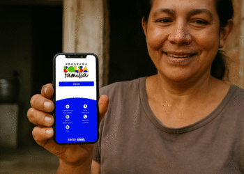 Pessoa segurando o celular com o aplicativo do Bolsa Família, destacando a opção de acesso ao calendário de pagamentos e informações sobre o programa.