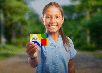 Menina sorridente mostrando o cartão do Programa Bolsa Família, anunciando pagamento extra de agosto para beneficiários com NIS final 1 a 5.
