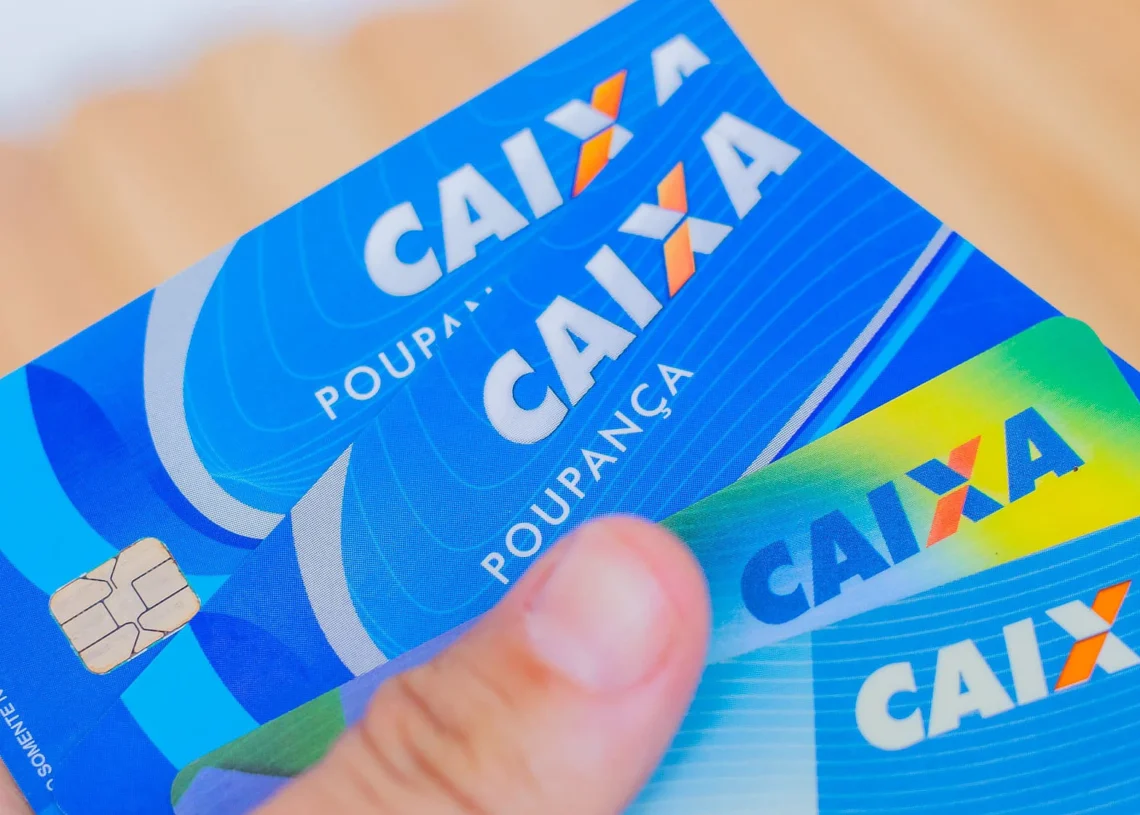 Cartões da Caixa Econômica Federal sendo segurados, mostrando suas cores e design. Importante para entender a diferença entre números de agência e conta. 