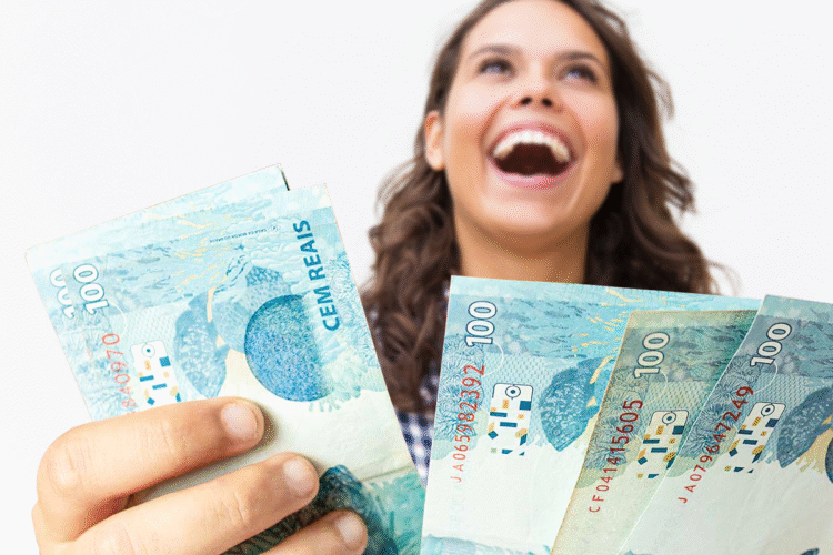 Pessoa sorrindo e segurando notas de 100 reais, representando o resgate do abono salarial não sacado.