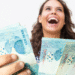 Pessoa sorrindo e segurando notas de 100 reais, representando o resgate do abono salarial não sacado.