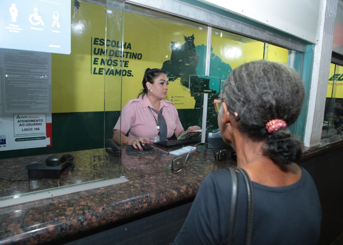 Pessoa idosa sendo atendida no guichê de vendas de passagens interestaduais, com a atendente no balcão. A Carteira do Idosa é apresentada como comprovante para obter desconto ou gratuidade nas passagens.