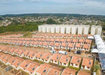 Imagem aérea de um conjunto habitacional com casas térreas e prédios ao fundo, representando o programa Minha Casa, Minha Vida.
