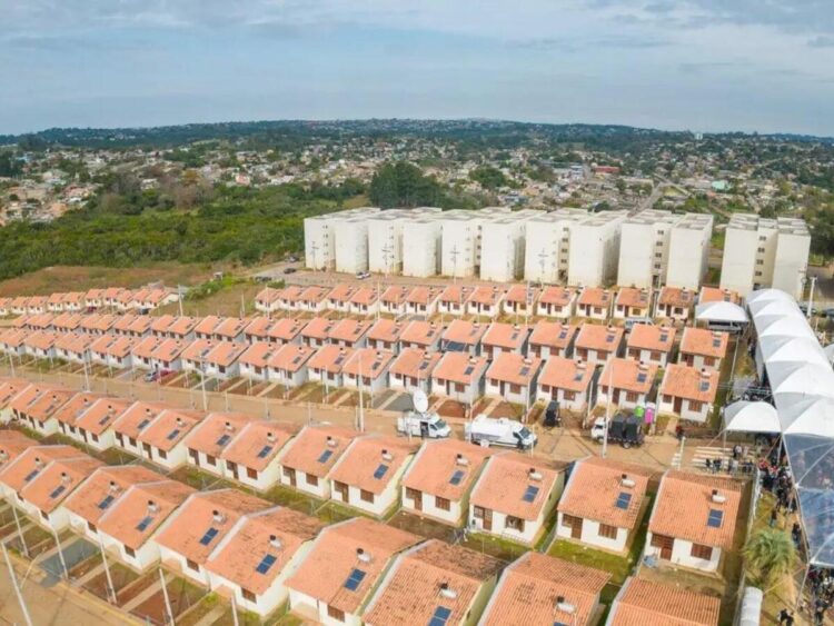 Imagem aérea de um conjunto habitacional com casas térreas e prédios ao fundo, representando o programa Minha Casa, Minha Vida.