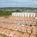 Imagem aérea de um conjunto habitacional com casas térreas e prédios ao fundo, representando o programa Minha Casa, Minha Vida.