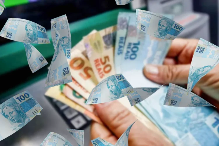 Imagem de uma mão segurando várias notas de R$ 100 e R$ 50 com um fundo desfocado de um caixa eletrônico, simbolizando o pagamento do programa Pé-de-Meia