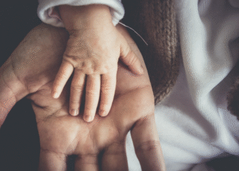 Imagem de uma mão de adulto segurando a mão de um bebê, simbolizando o reconhecimento de paternidade.