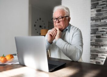 Aposentado usando notebook enquanto anota informações para gerar renda extra