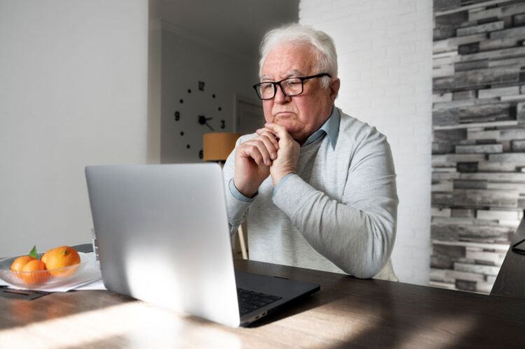 Aposentado usando notebook enquanto anota informações para gerar renda extra