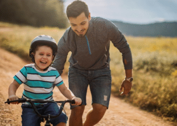 Pai ajudando filho a andar de bicicleta, representando apoio e cuidado.