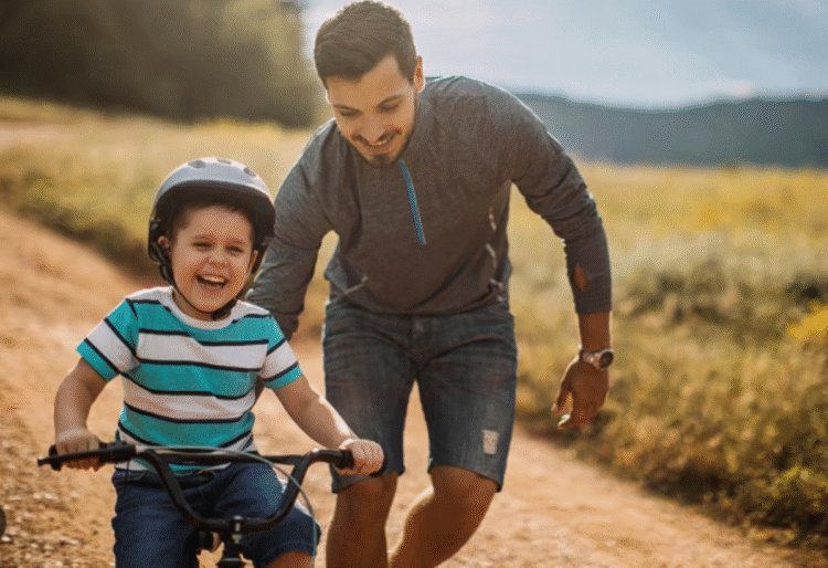 Pai ajudando filho a andar de bicicleta, representando apoio e cuidado.