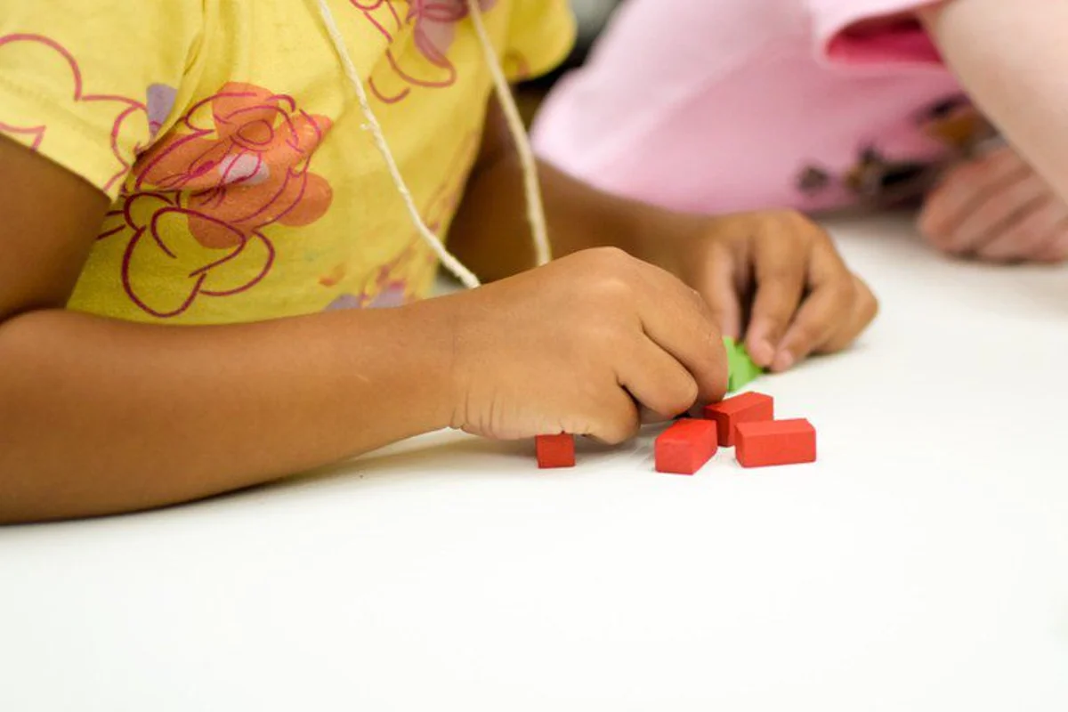 Criança manipulando peças de blocos coloridos, representando a inclusão e o apoio do programa BPC na Escola.