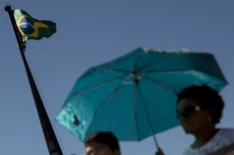 Cidadãos com guarda-sol sob a bandeira do Brasil em dia ensolarado