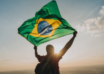 Pessoa segurando a bandeira do Brasil ao pôr do sol, simbolizando retorno ao país
