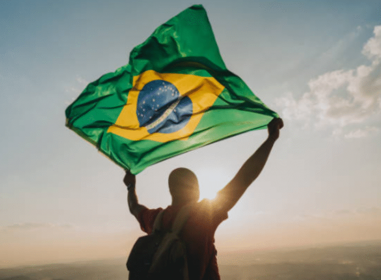 Pessoa segurando a bandeira do Brasil ao pôr do sol, simbolizando retorno ao país