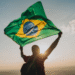 Pessoa segurando a bandeira do Brasil ao pôr do sol, simbolizando retorno ao país
