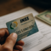 Mão segurando cartão do INSS sobre documentos em uma mesa