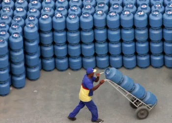 Funcionário transportando botijão de gás, parte de uma grande quantidade de cilindros prontos para distribuição.