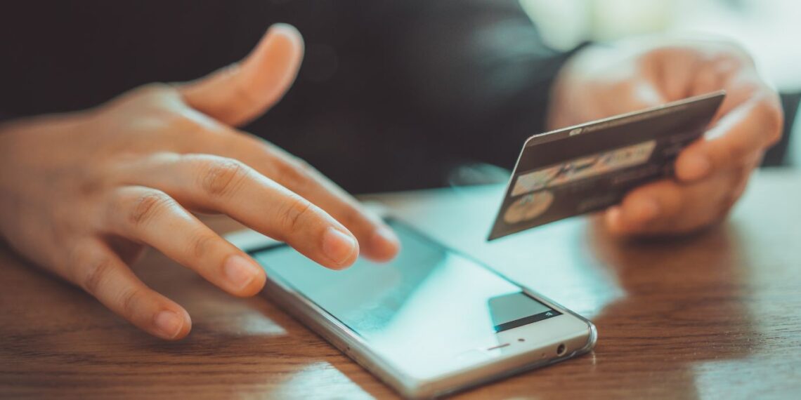 Pessoa usando cartão de crédito para pagamento online, representando o golpe da taxa falsa