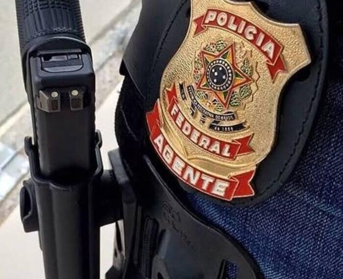 Distintivo dourado da polícia federal com arma na cintura.