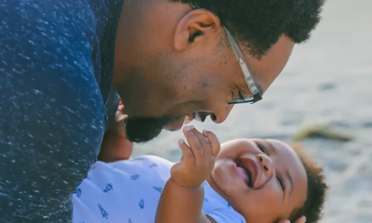 Pai sorrindo enquanto segura seu bebê nos braços, representando vínculo afetivo e direitos garantidos
